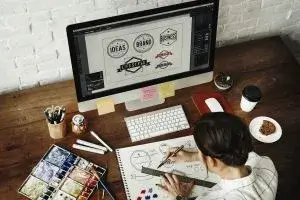 Graphic designer creating professional logo and brand identity: sketching concepts by hand, using watercolor, and refining designs in Adobe Illustrator on iMac workstation